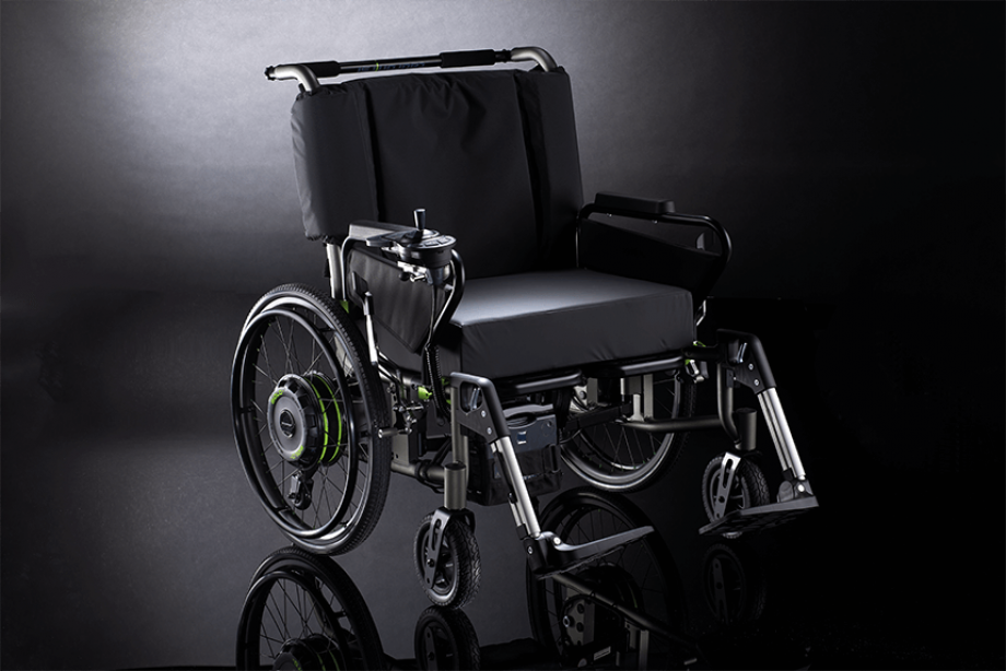 The picture shows an XXL wheelchair Tauron RSI of the company Dietz with attached add-on drive SOLO+ of the company AAT. The SOLO+ is designed for bariatric patients and fits very well to the black Tauron with its black design.