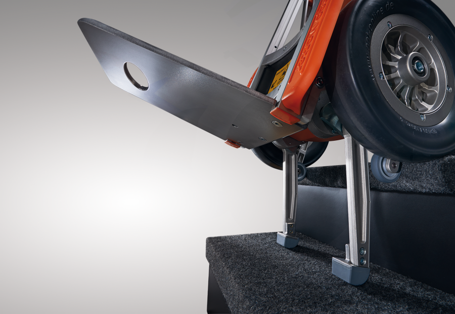 Das Bild zeigt den Steigvorgang der Treppenhilfe c-max. Die Steigbein sind ausgefahren und setzen bereits auf der unteren Treppenstufe auf. Die Sicherheitsbremsen, welche am großen Laufrad befestigt sind, setzen am Stufenrand auf und schützen so vor einem abwärtsrollen.