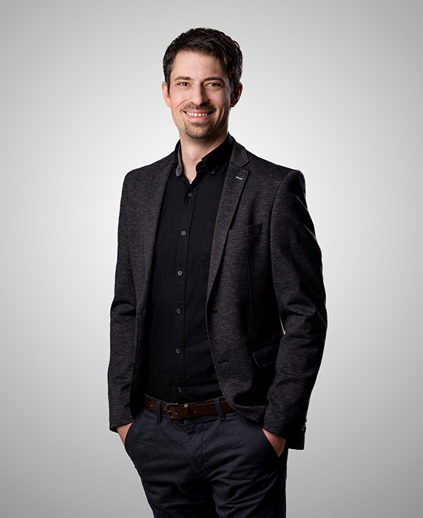 Auf dem Foto ist der Schulungsleiter von AAT Mark Retter zu sehen. Er steht vor einer grauen Wand und trägt ein dunkles Hemd mit dunklem Sakko. Er lächelt freundlich in die Kamera.