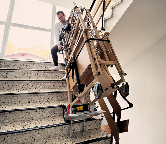 Einzelperson befördert mithilfe des Treppensteigers CC160 RE mühelos ein Pflegebett die Treppe hinab – kraftsparend und sicher