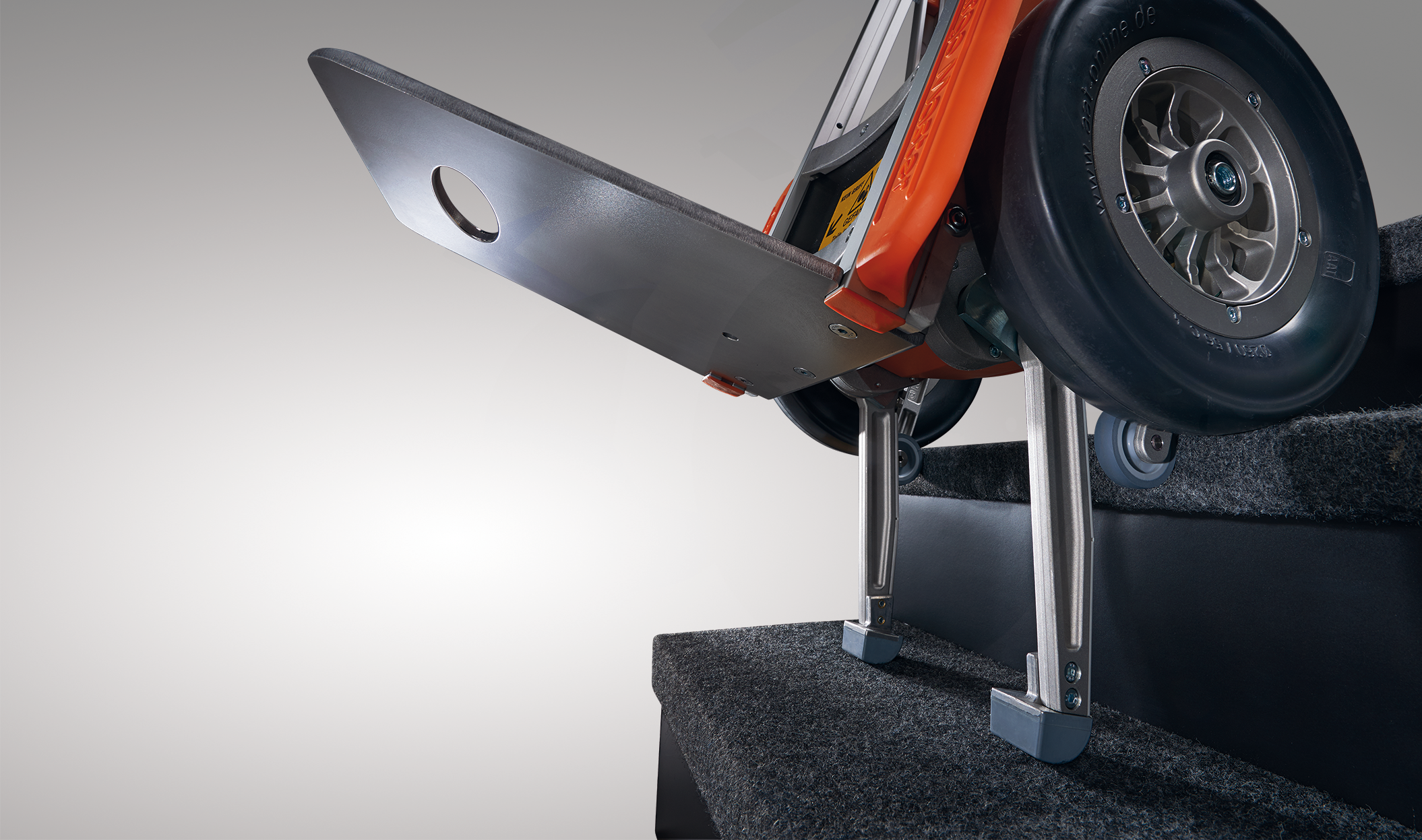 Das Bild zeigt den Steigvorgang der Treppenhilfe c-max. Die Steigbein sind ausgefahren und setzen bereits auf der unteren Treppenstufe auf. Die Sicherheitsbremsen, welche am großen Laufrad befestigt sind, setzen am Stufenrand auf und schützen so vor einem abwärtsrollen. 