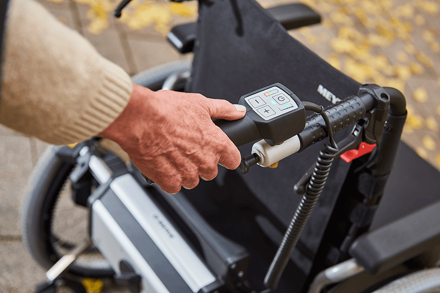 Das Bild zeigt einen Detailausschnitt einer Schiebe- und Bremshilfe V-MAX². Zu sehen ist der Bediengriff der Schiebehilfe mit einigen Funktionen, wie dem EIN/AUS-Schalter, Akkuanzeige und Geschwindigkeitseinstellung.