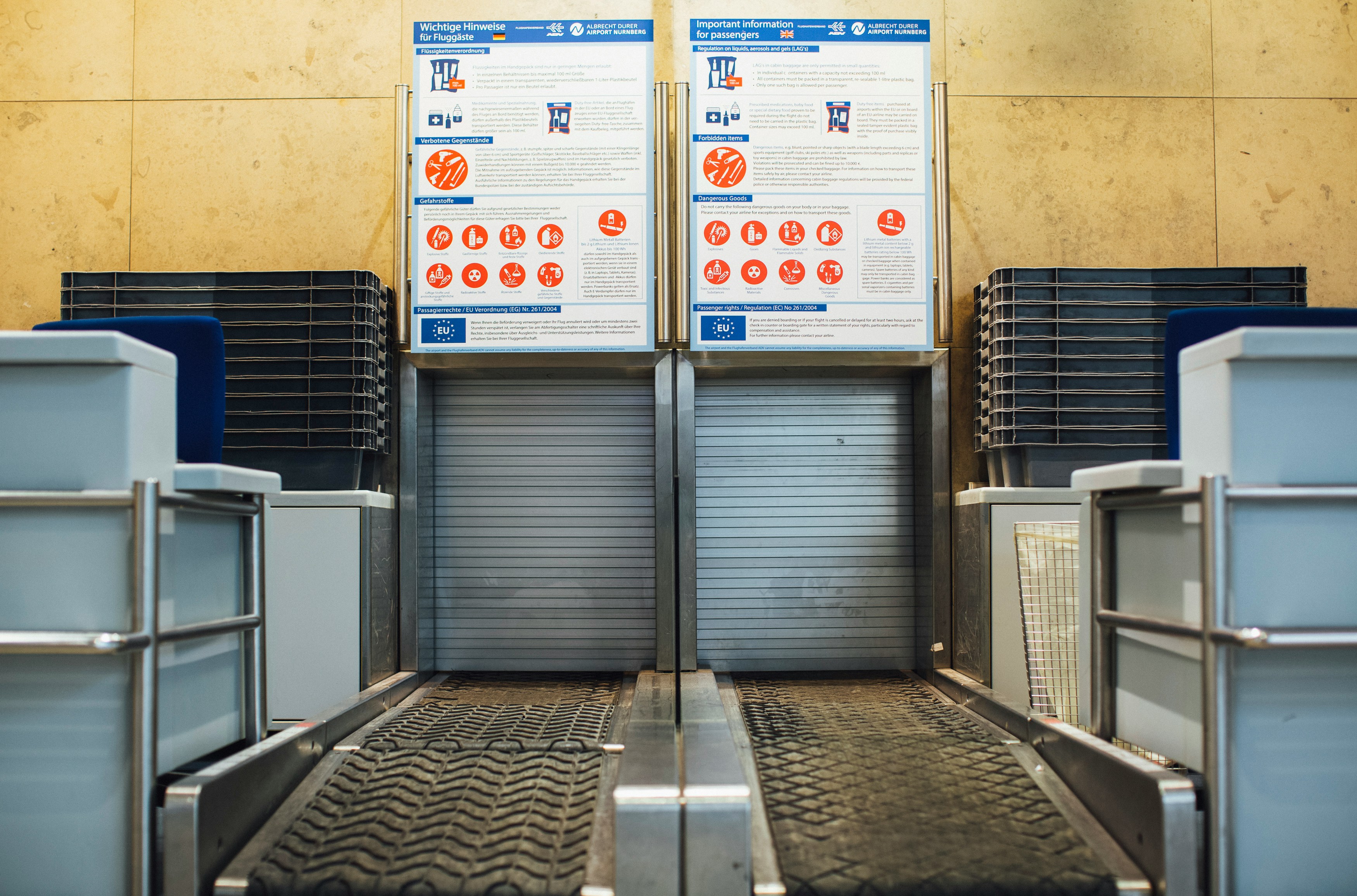 Das Bild zeigt die Gepäckabgabe eines Flughafens. Hinter den Beförderungsbändern für das Gepäck befinden sich Hinweisplakate über das Mitführen von Artikeln. Lithium-Ionen Akkus von Elektrorollstühlen oder Zusatzantrieben haben strengere Richtlinien.