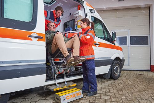 Das Bild zeigt zwei Mitarbeiter eines Rettungsdienstunternehmens, welche einen Mann in einem mobilen Treppensteiger CR23 mit integrierter Sitzeinheit aus einem KTW transportieren.