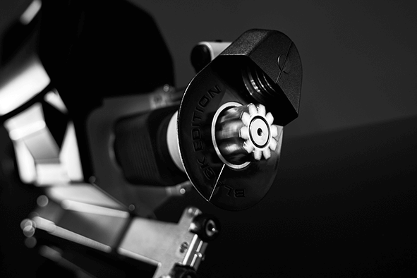 The picture shows a detailed view of the MAX-E wheelchair drive. You can see the drive unit and a rotating drive shaft, which drives the wheelchair wheel via a sprocket. 