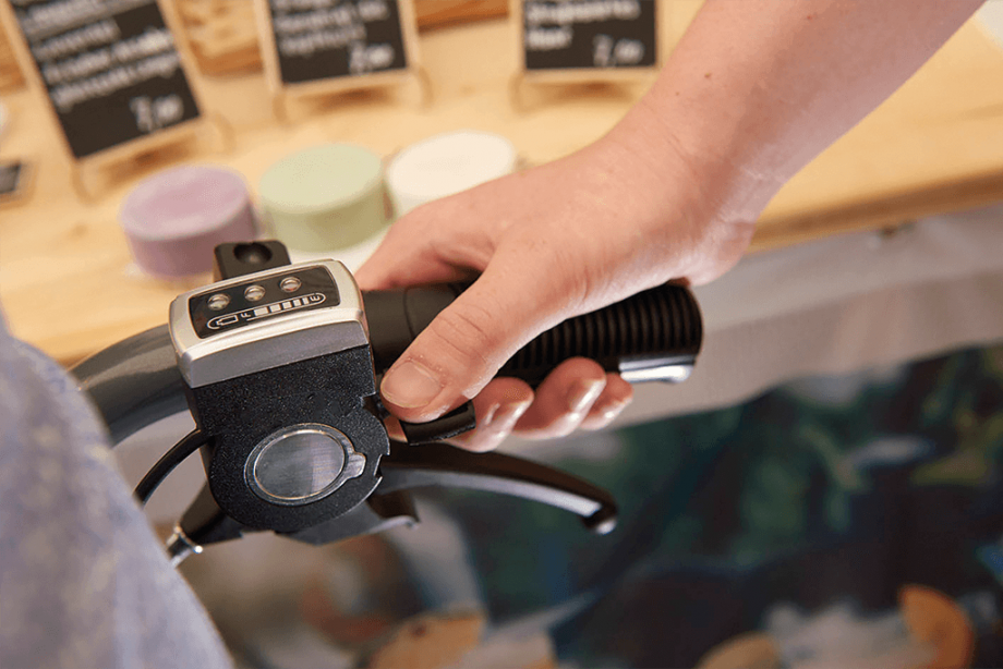 Das Bild zeigt eine Detailaufnahme des Rollstuhlgriffs mit dem angebrachten Bedienteil der Schiebehilfe V-MAX mini und die Hand der jungen Frau, die den Rollstuhl hält. Sie kann das Bediengerät der Antriebshilfe mit einer Hand einfach bedienen. 