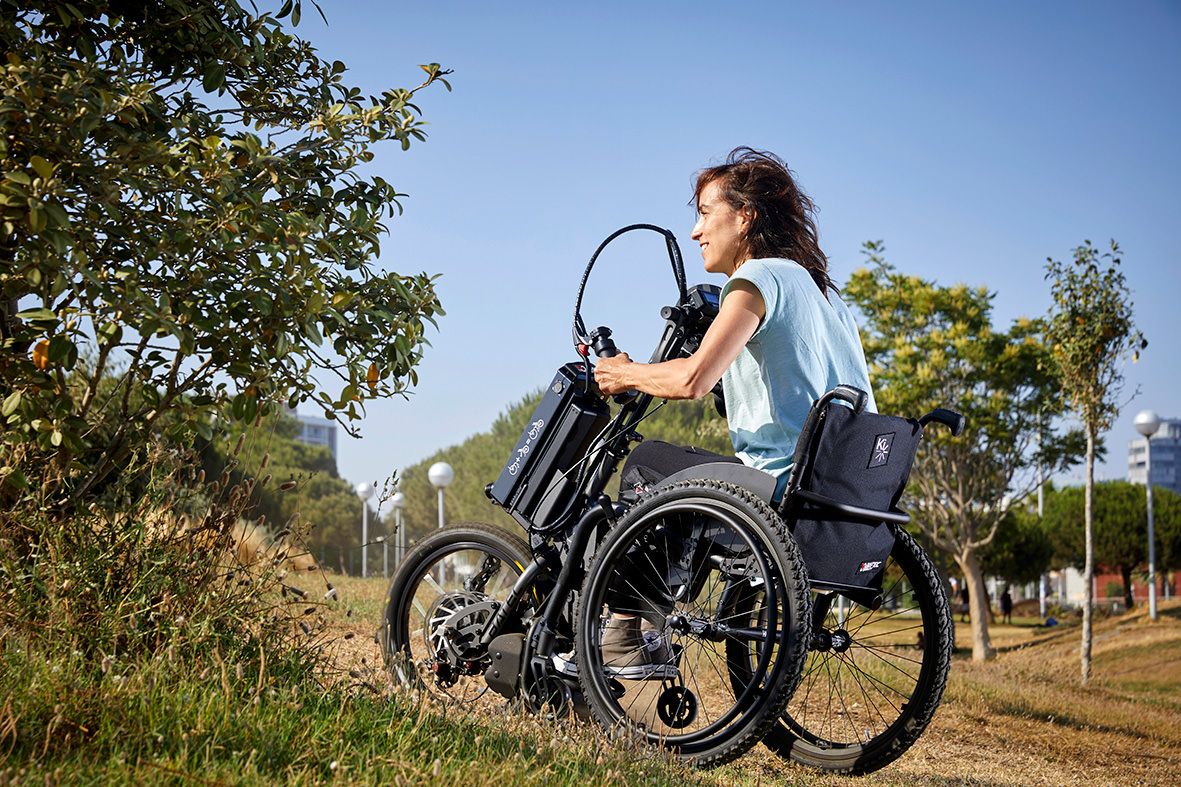 Das Bild zeigt eine sportliche junge Frau im Rollstuhl, die mit einem Handbike draußen einen Hang nach oben fährt.