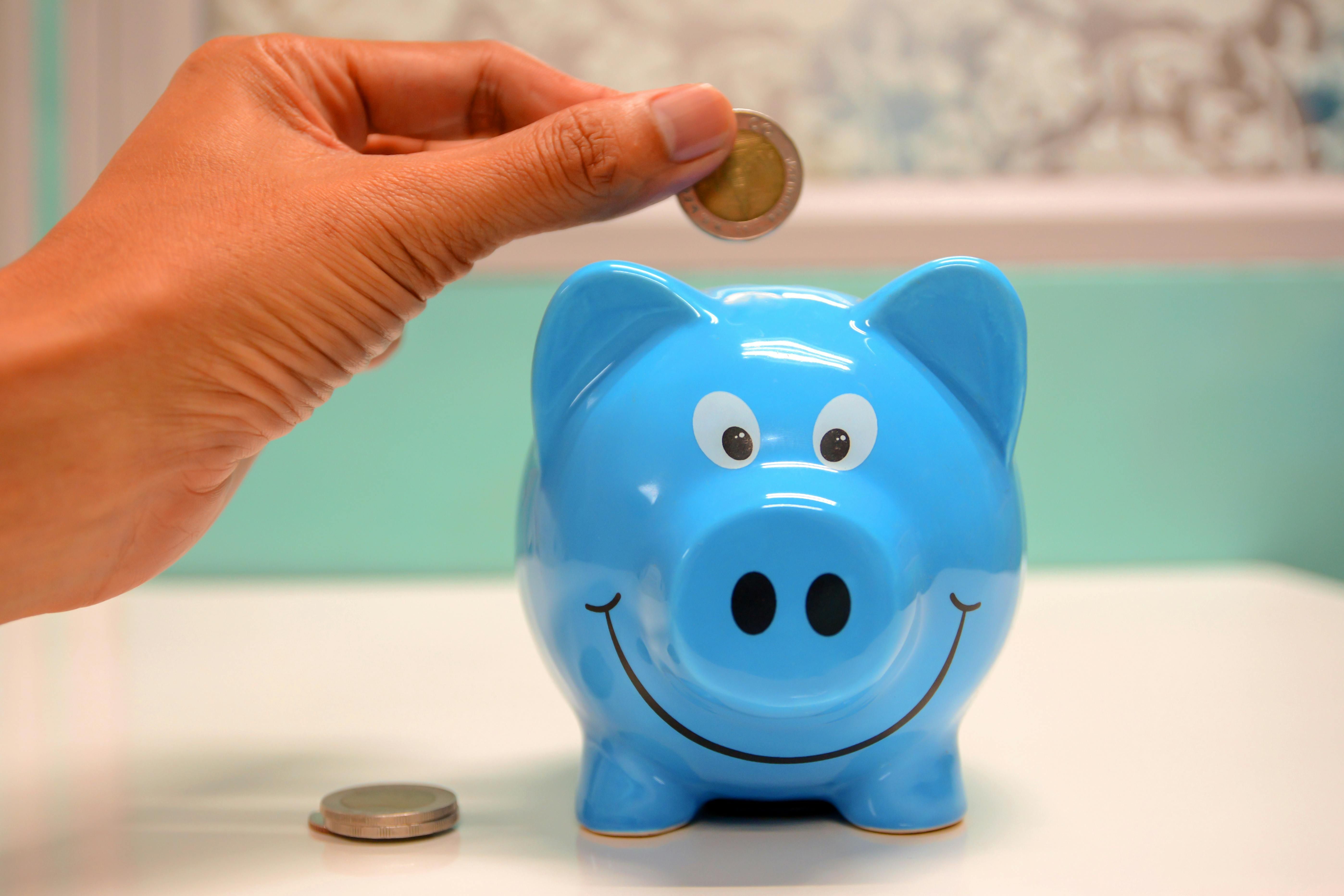 Das Bild zeigt ein blaues Sparschwein und eine Hand, welche eine Münze hineinwirft. Das zu füllende Sparschwein symbolisiert die Finanzierungsunterstützungen bei einer Hilfsmittelversorgung. 