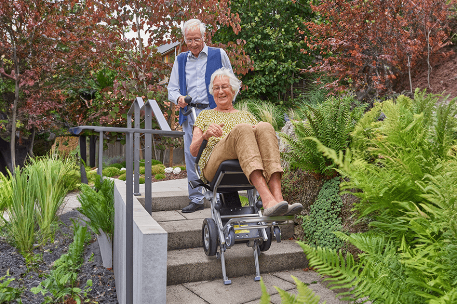Das Bild zeigt einen älteren Herrn, der im Treppensteiger sitzt und eine Frau, die den Treppensteiger bedient. 